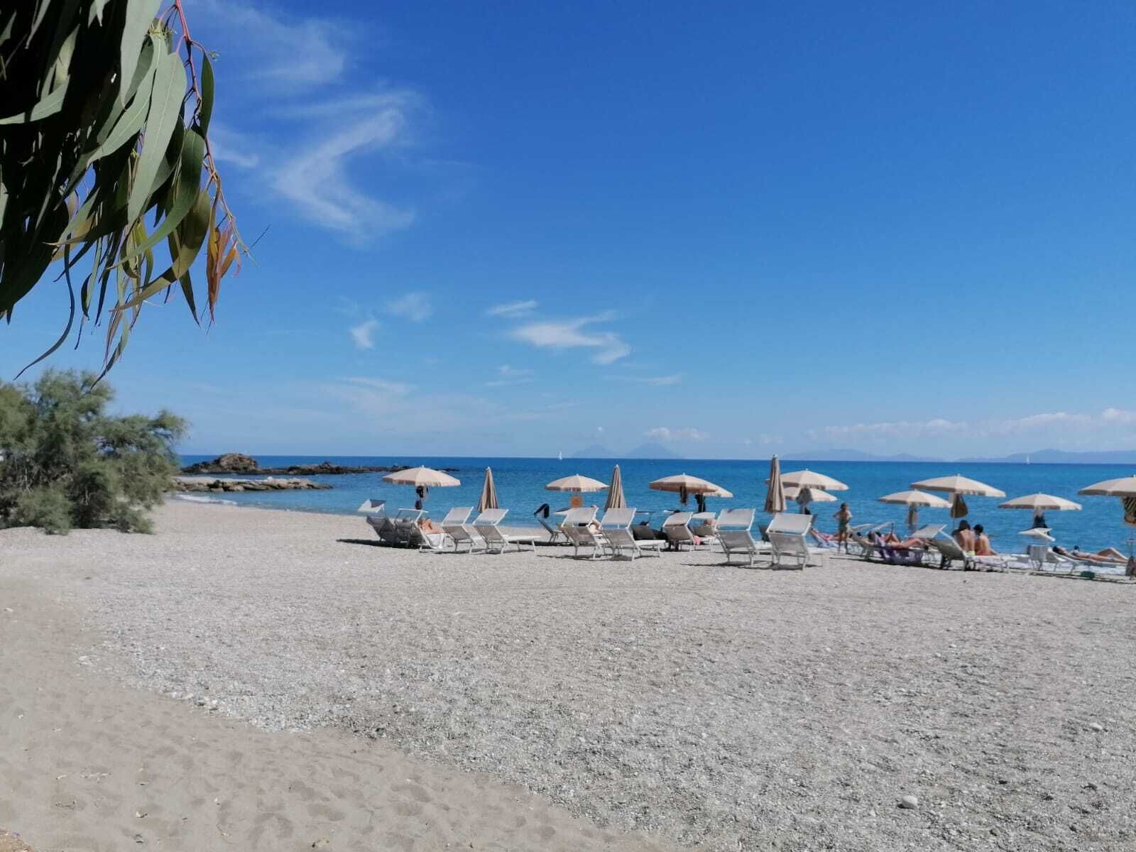 Una spiaggia con lettini e ombrelloni, cielo sereno e l'oceano sullo sfondo.