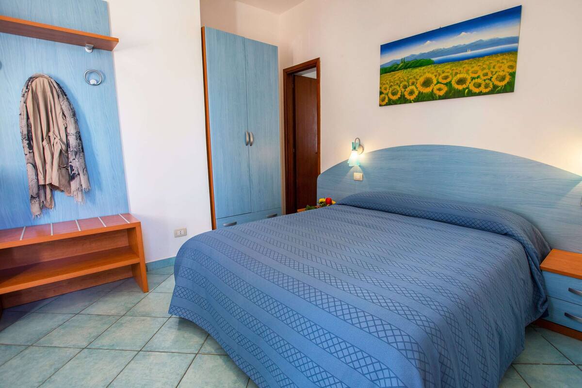 Un dormitorio con una cama, un banco de madera, una puerta y un cuadro en la pared.
