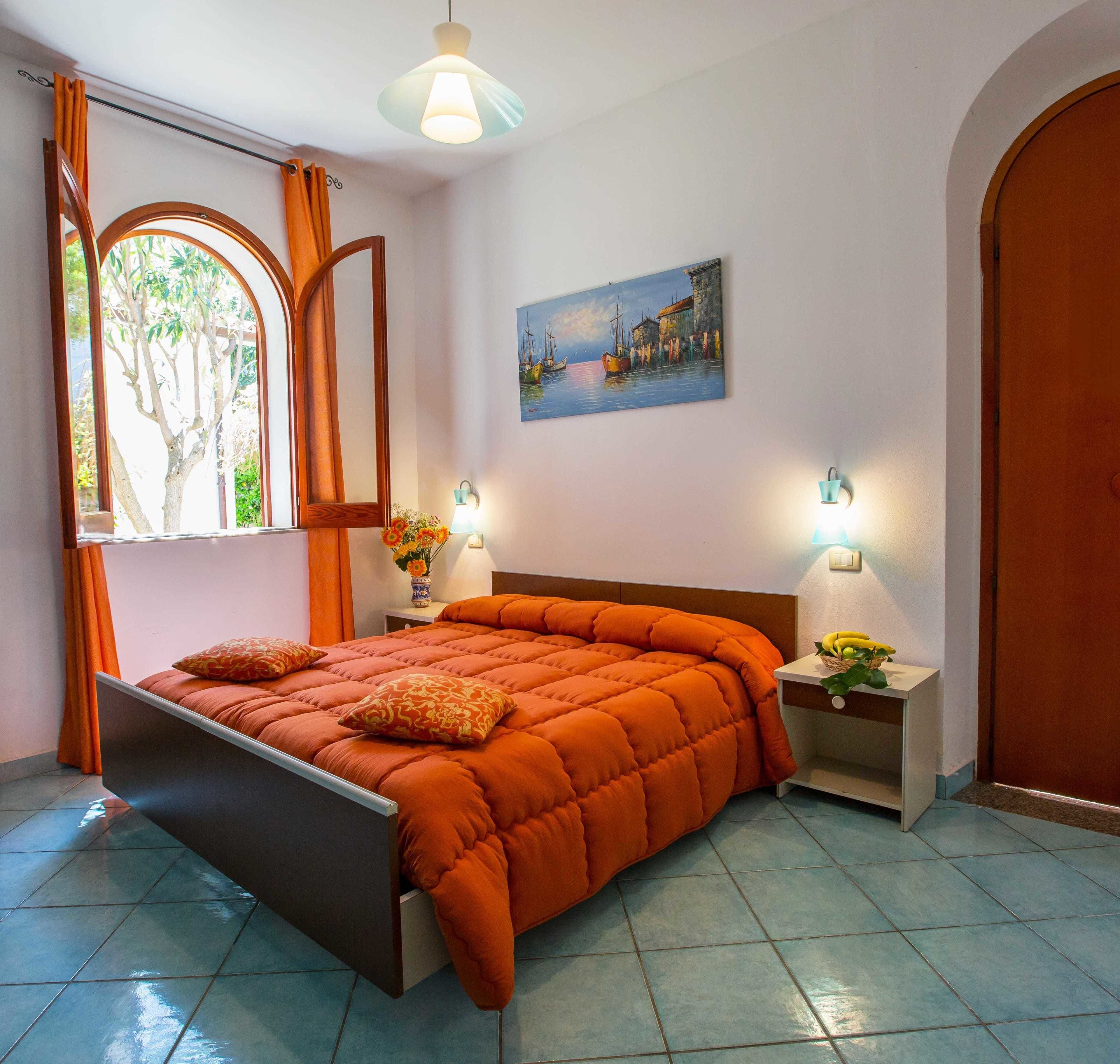 A bedroom with a bed, two bedside tables, a window with curtains, a painting on the wall, and a door.
