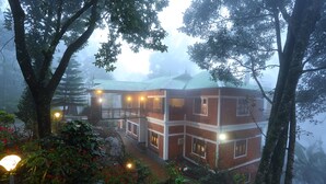 A multi-story building with a brick exterior and multiple windows, surrounded by dense foliage and trees. - Madhumanthra Resort (Devikolam)
