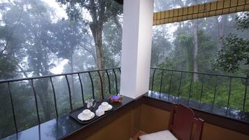 A balcony with a view of a forest. There is a table with a tray of items, including plates and a bowl.