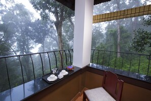 A balcony with a view of a forest. There is a table with a tray of items, including plates and a bowl. - Madhumanthra Resort (Devikolam)