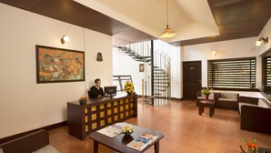 A reception area with a desk, chairs, a staircase, and a painting on the wall. - Madhumanthra Resort (Devikolam)