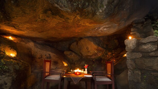 A cave dining area with a table set for four, surrounded by stone walls and illuminated by small lights. - Madhumanthra Resort (Devikolam)