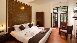 A hotel room with a large bed, a desk with a chair, a television, and a window with curtains. - Madhumanthra Resort (Devikolam)