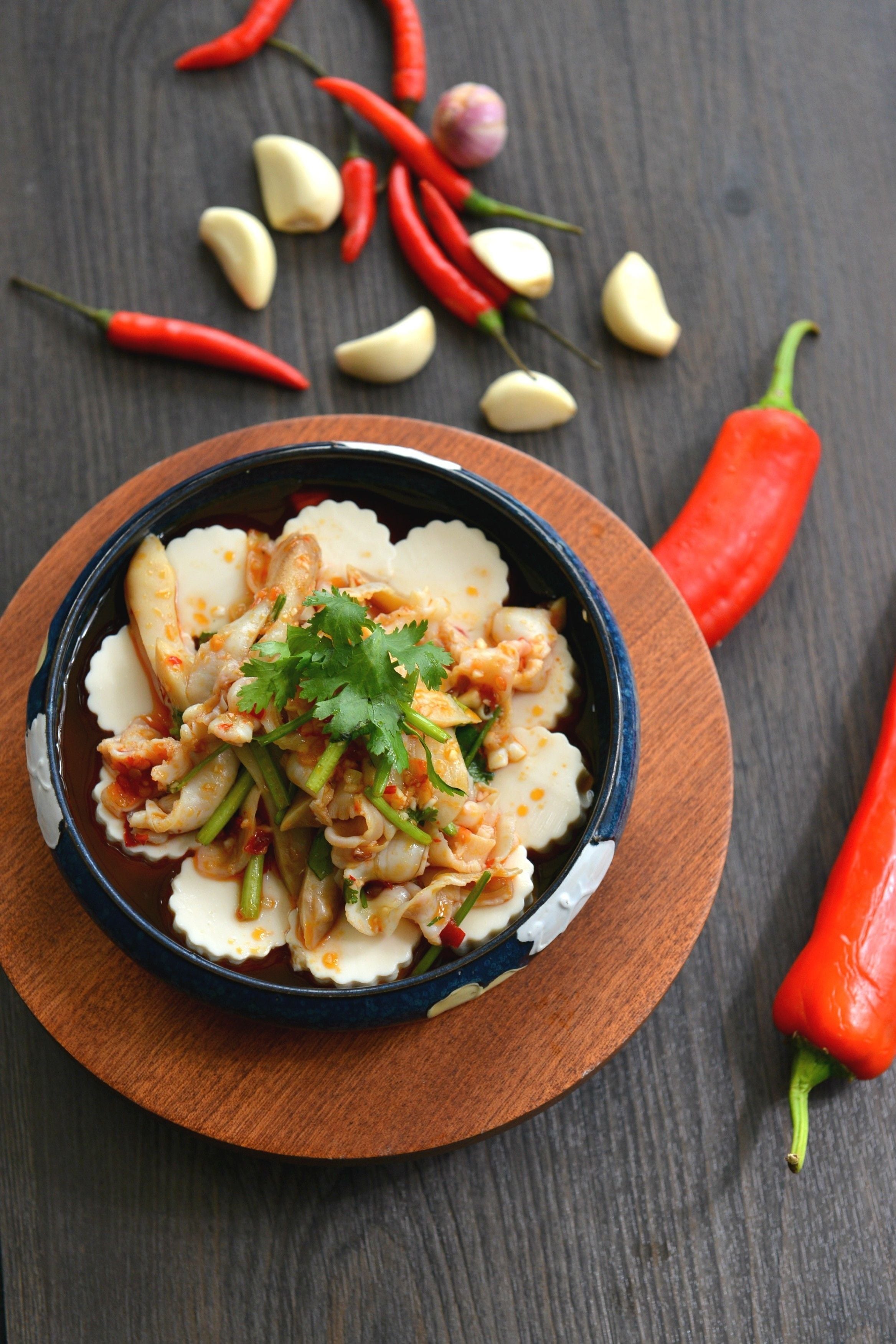 Un bol de comida sobre una tabla de madera, rodeado de chiles rojos y dientes de ajo.