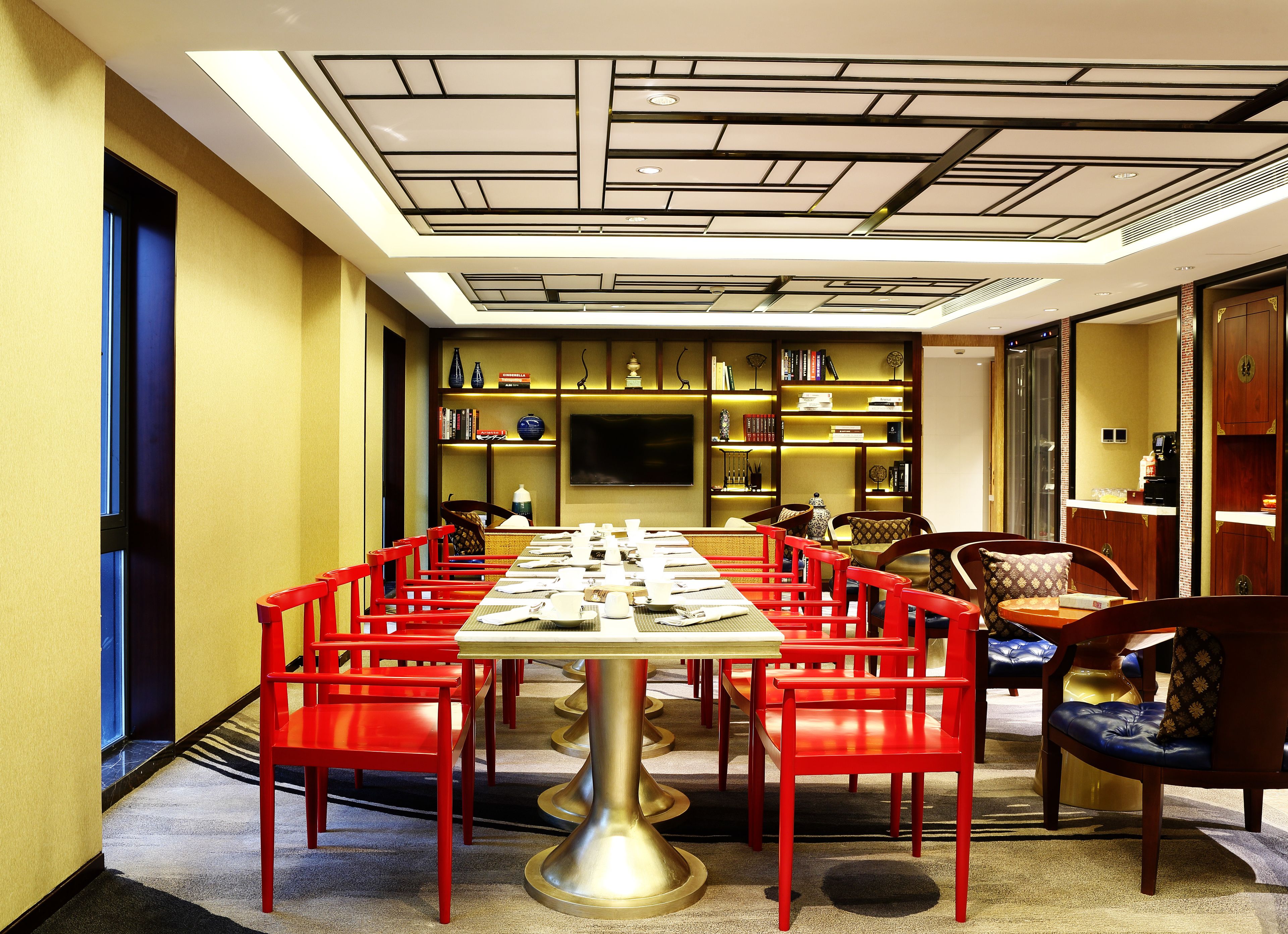 A conference room with a long table, red chairs, and a modern ceiling design.
