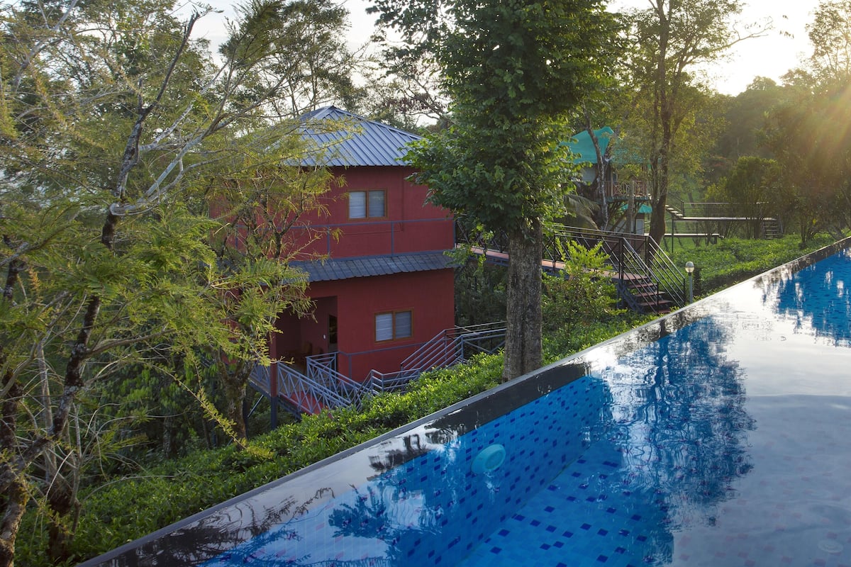 Ein Swimmingpool mit einem roten Gebäude im Hintergrund, umgeben von Bäumen.