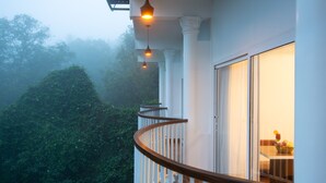 Un balcon doté de balustrades blanches et d’une main courante en bois, offrant une vue sur une forêt verdoyante et luxuriante.