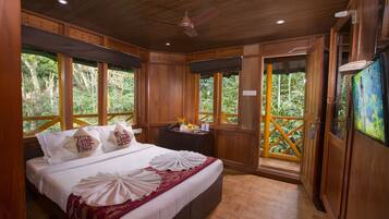 A wooden room with a large bed, wooden ceiling, and windows overlooking a lush garden.
