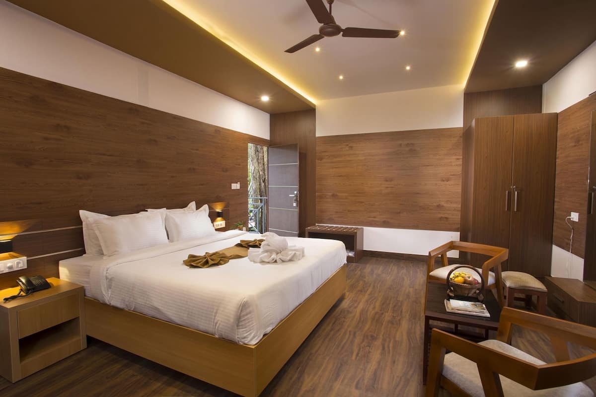 Ein modernes Hotelzimmer mit einem großen Bett, Holzwänden, einem Deckenventilator und einer kleinen Sitzecke mit Tisch und Stühlen.