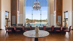 Eine großzügige Lobby mit weitreichendem Blick auf Pool und Strand, inklusive Kronleuchter, rundem Tisch mit dekorativer Tischdekoration und mehreren Sesseln.