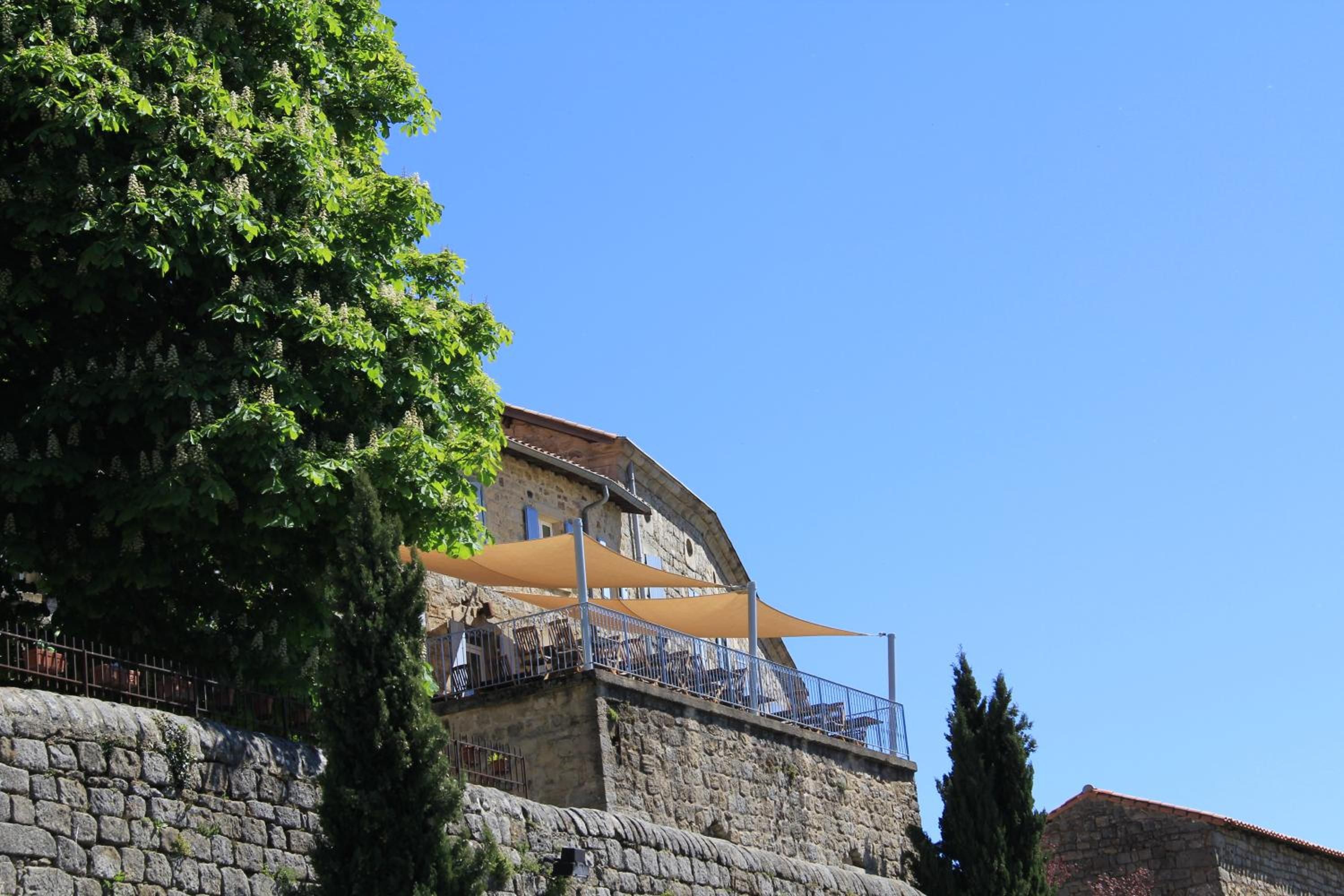 A stone building with a balcony overlooking a body of water, surrounded by greenery.