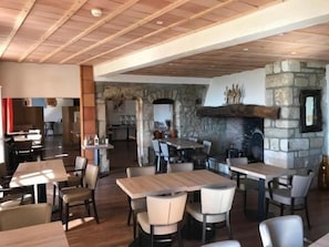 Un restaurante con mesas y sillas de madera, una chimenea de piedra y una zona de cocina al fondo.