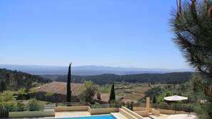 Una piscina con sillones de playa y sombrillas, rodeada de una vista panorámica de montañas y árboles.