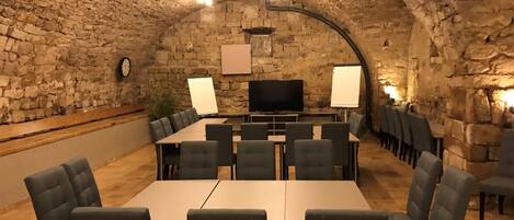 Una sala de conferencias con una larga mesa y sillas, paredes de piedra y una pantalla de televisión.