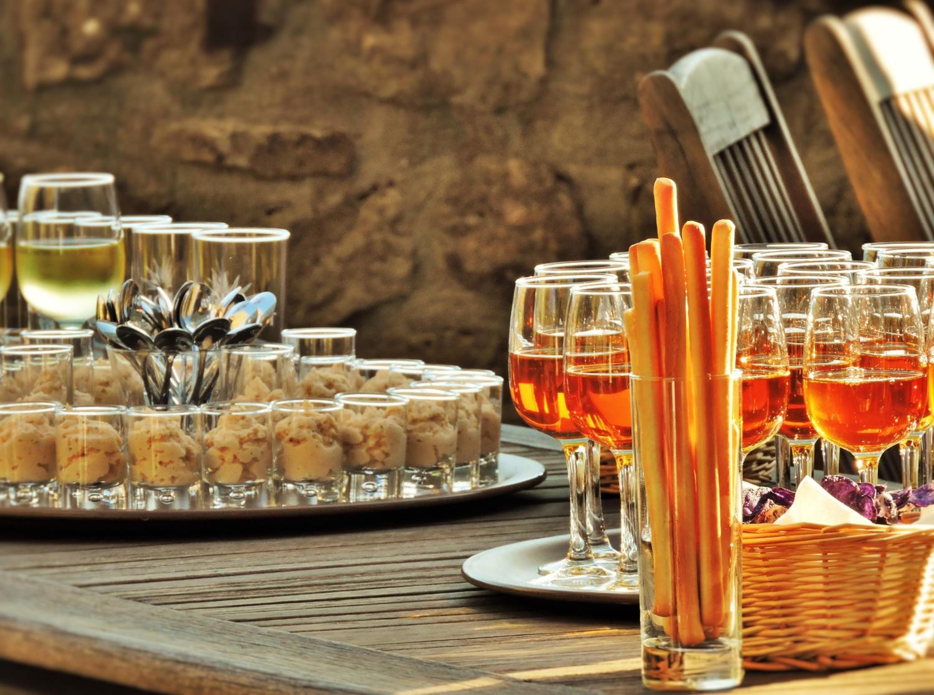 A table with glasses of amber liquid, possibly wine, and a tray of food items.