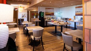 Un comedor moderno con mesas y sillas de madera, una estación de café y obras de arte en las paredes.