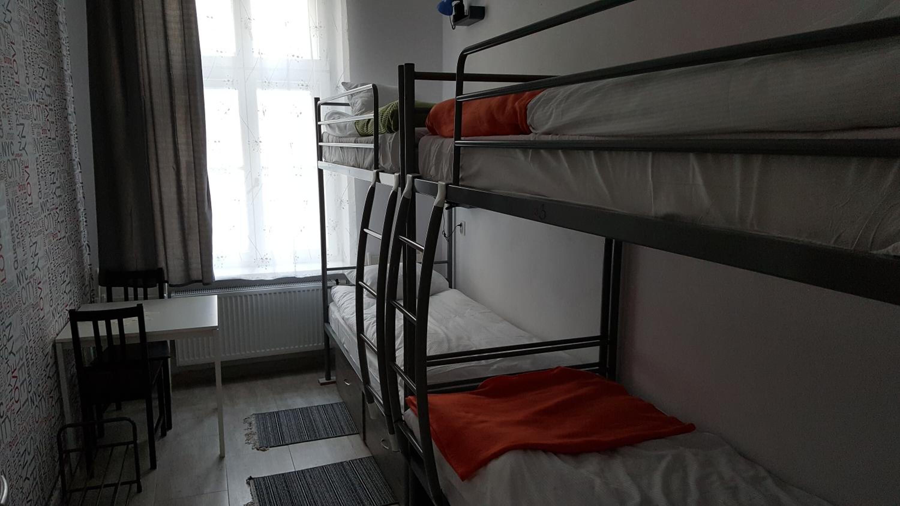 A dormitory room with bunk beds, a desk, and a radiator.