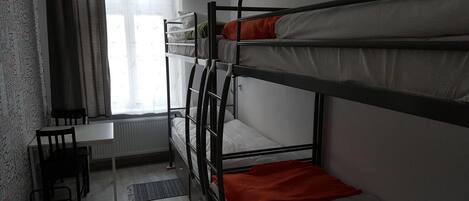 A dormitory room with bunk beds, a desk, and a radiator.