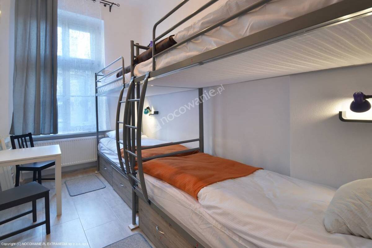 A bunk bed room with a desk and chair, a window with curtains, and a wall-mounted light fixture.