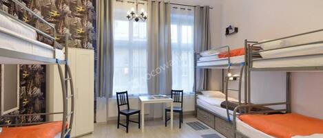 A dormitory room with bunk beds, a small table, chairs, and a chandelier.