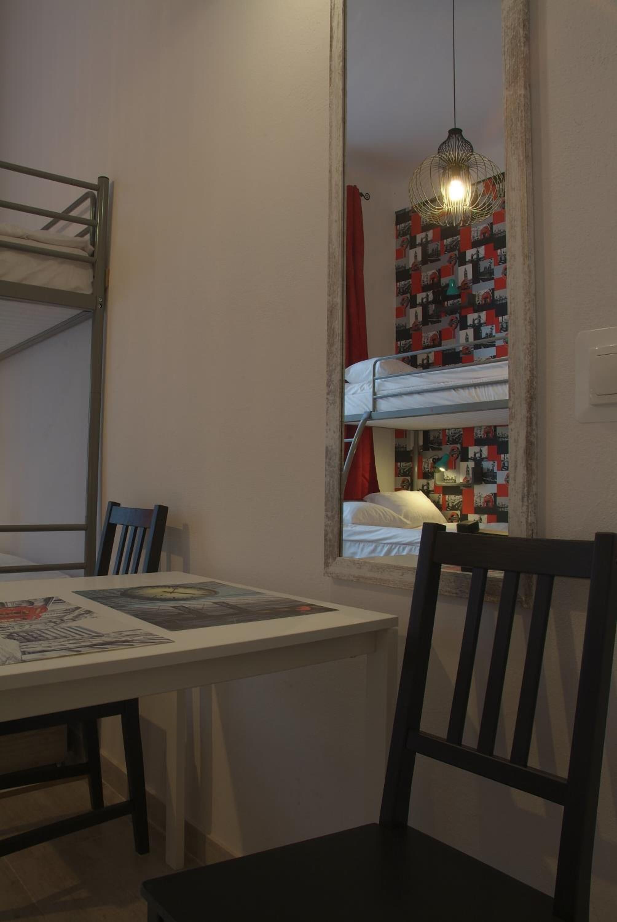 A bunk bed room with a table and chairs, a hanging light fixture, and a patterned wall.