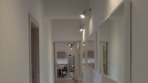 A narrow, well-lit hallway with a wooden floor, leading to a kitchen area with cabinets and appliances. - Hostel Lwowska 11 (Warsaw)