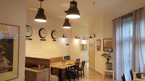 A modern kitchen with a dining area, featuring a brick wall, clocks, pendant lights, and a potted plant. - Hostel Lwowska 11 (Warsaw)