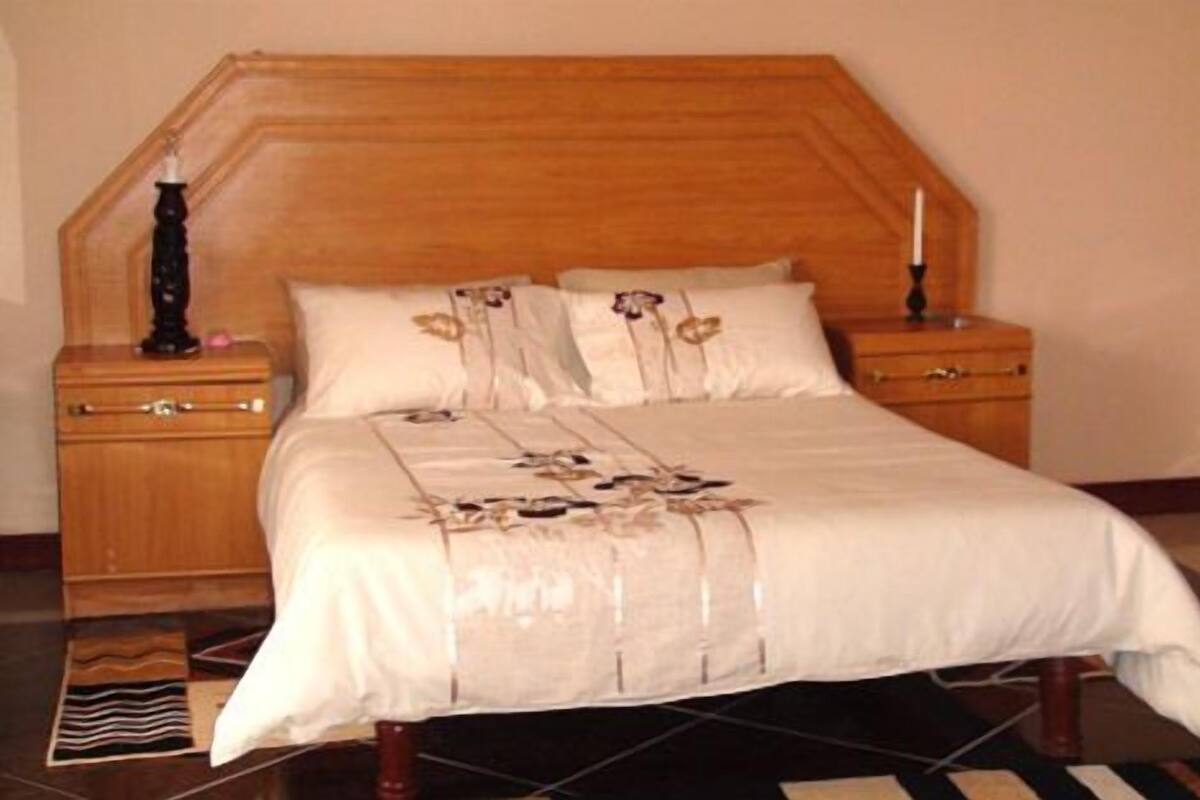 Quarto com cabeceira de madeira, duas mesas de cabeceira, cama com colcha floral e tapete listrado.