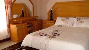 Ein Schlafzimmer mit einem hölzernen Kopfteil, einem Nachttisch mit Lampe, einem Schminktisch und einem Spiegel.