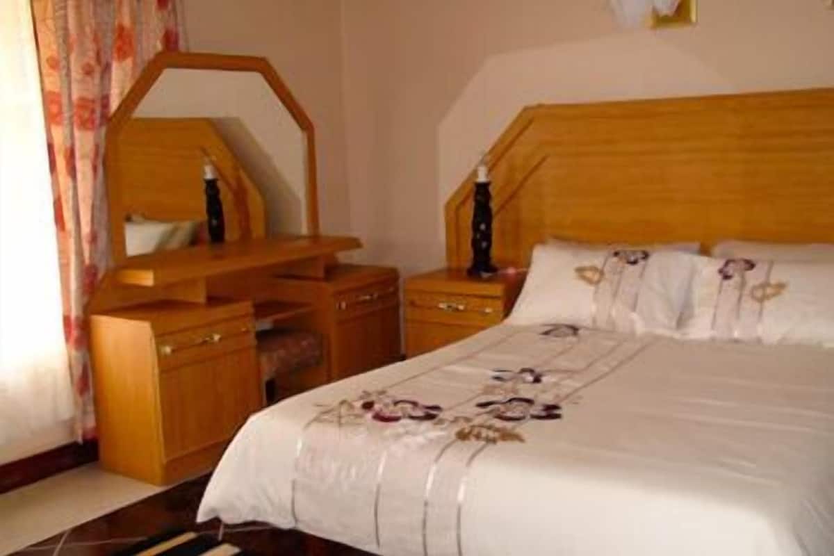 Um quarto com cabeceira de madeira, mesa de cabeceira com luminária, cômoda e espelho.