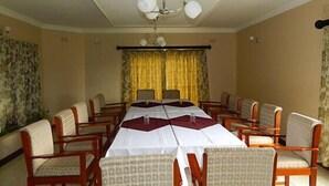 Ein Konferenzraum mit langem Tisch, mehreren Stühlen, einer Chandelierleuchtre und gelben Vorhängen.
