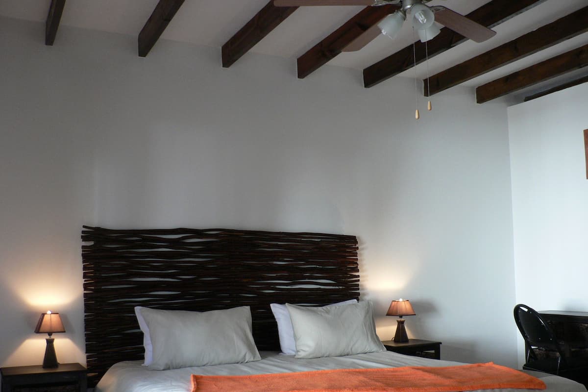Een slaapkamer met een houten hoofdeinde, twee bedlampen, een bed met witte beddengoed en een oranje plaid, en een plafondventilator.