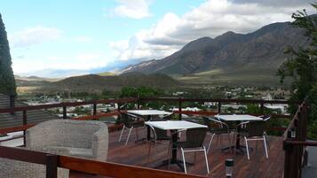 A deck with tables and chairs overlooking a mountainous landscape.