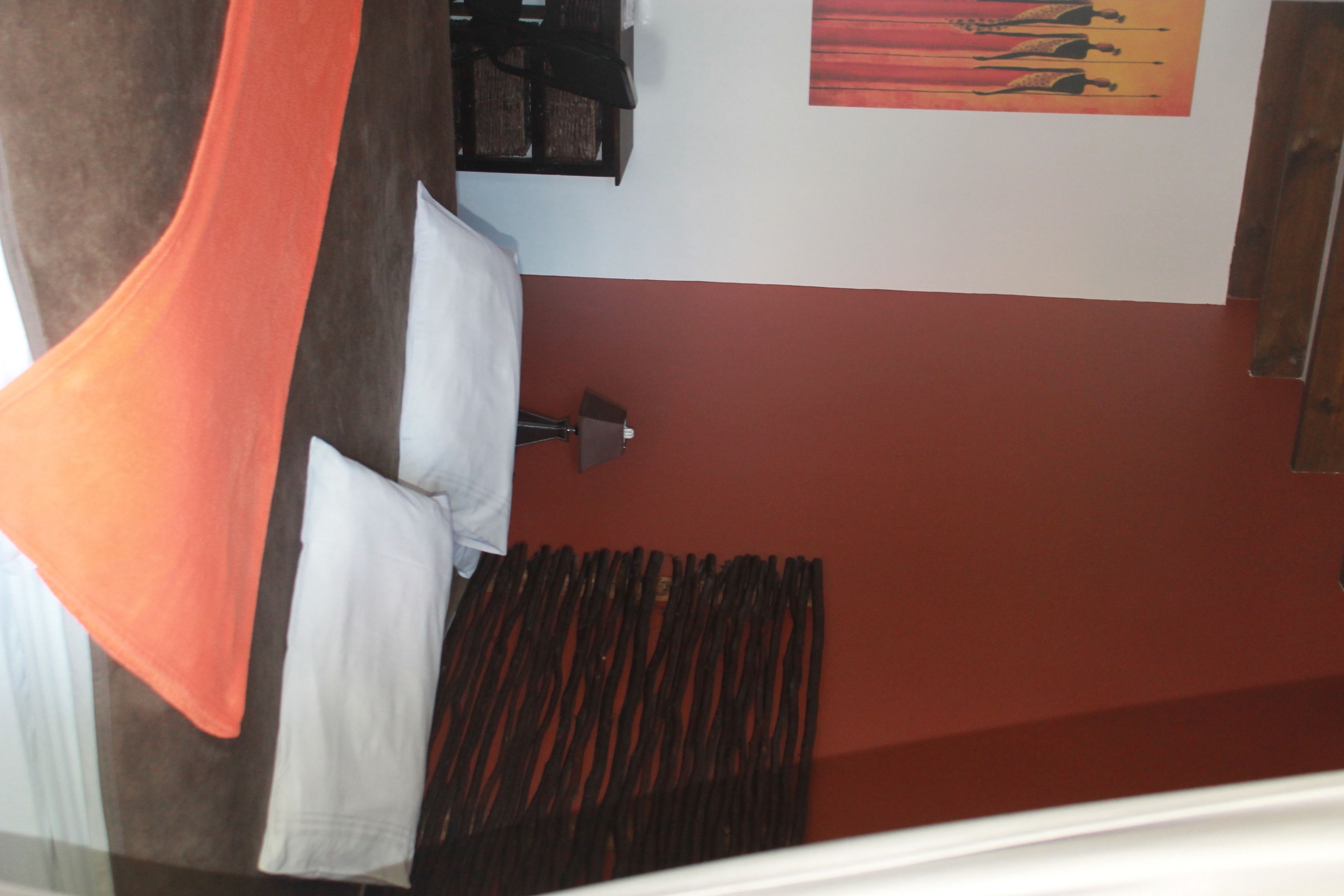 A room with a bed, a wall-mounted lamp, and a painting.