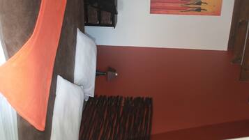 A room with a bed, a wall-mounted lamp, and a painting.
