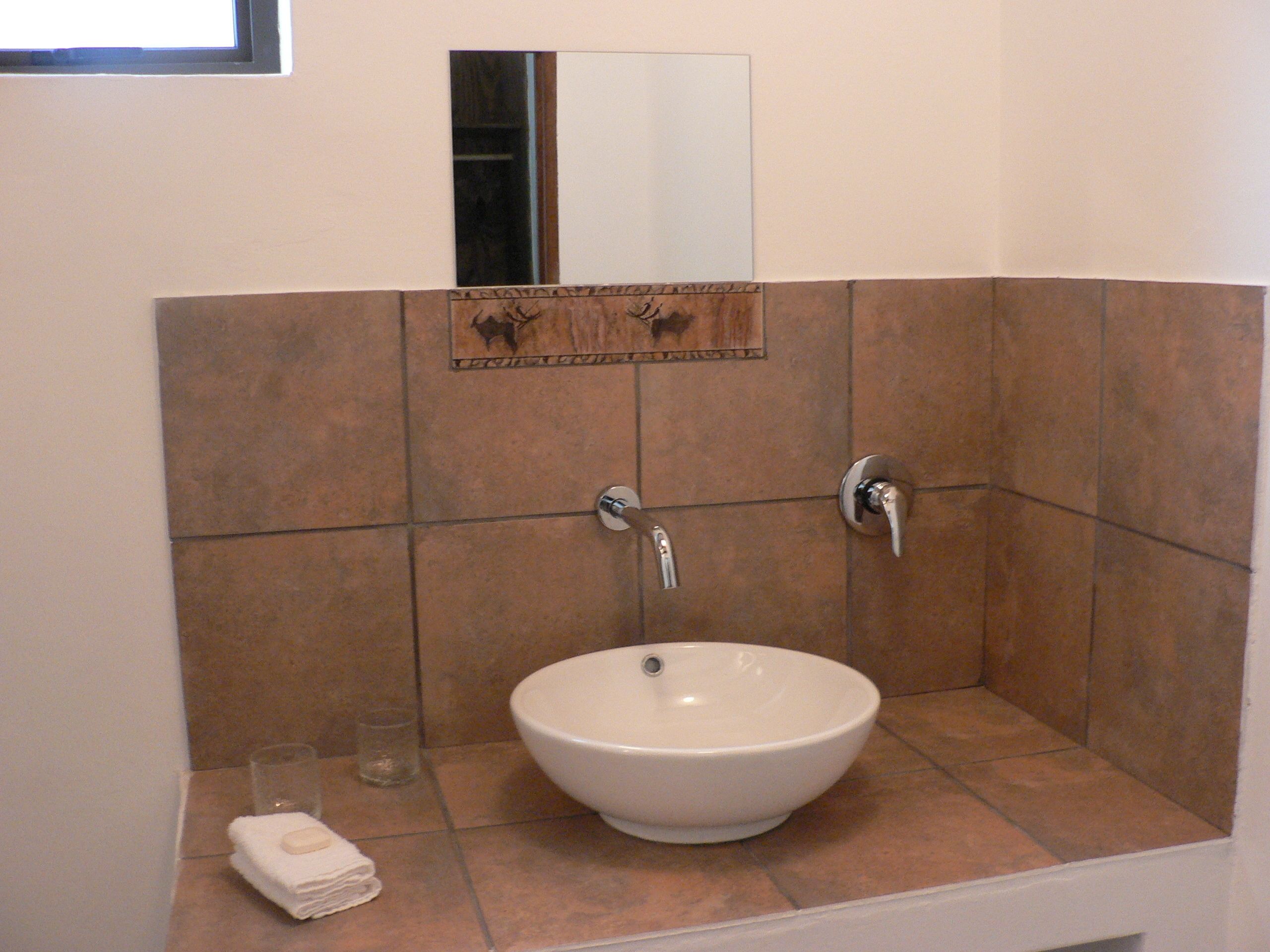 A bathroom with a white sink, two faucets, a glass, and a towel.