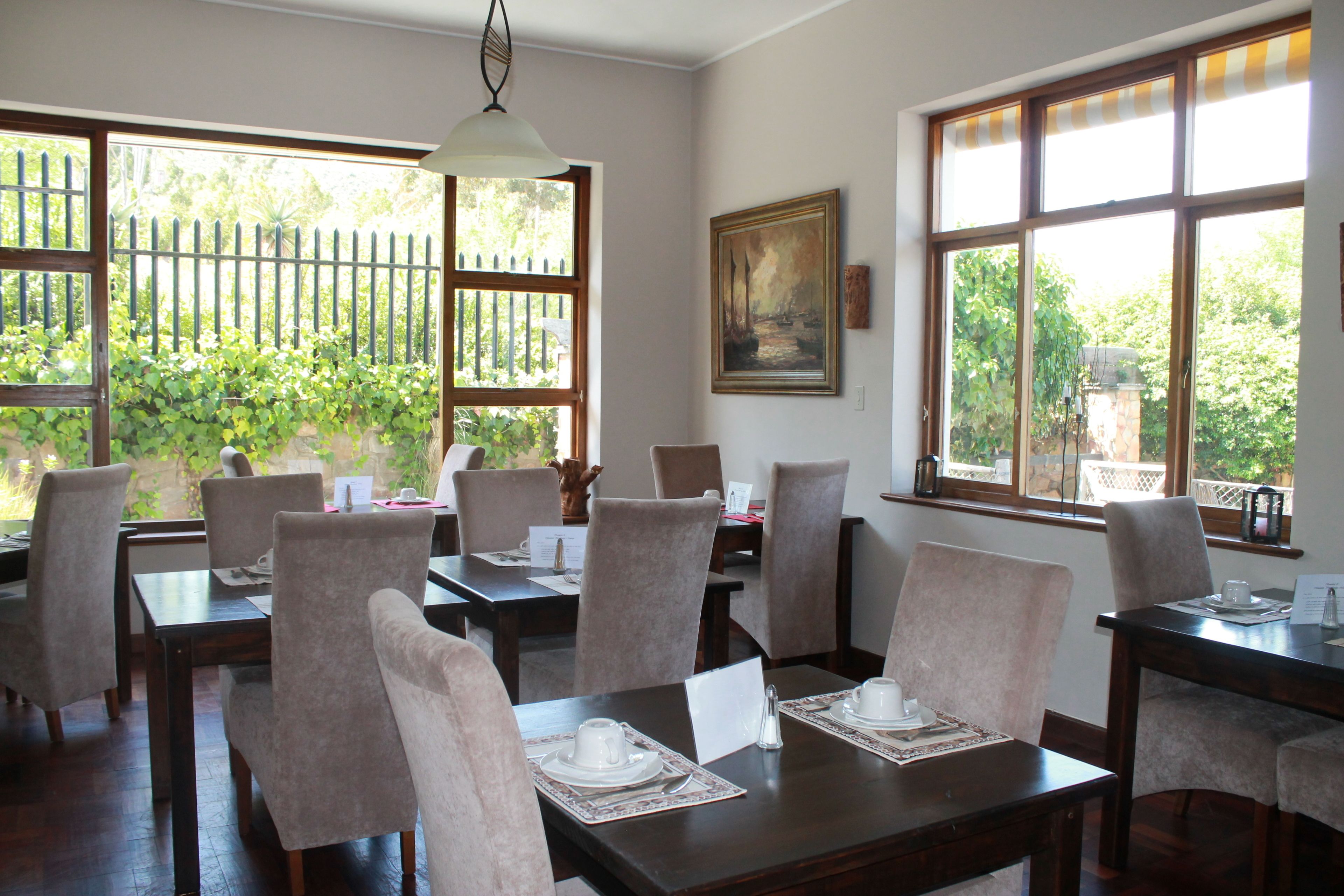 Un espace repas avec des tables disposées pour quatre personnes, des chaises et un tableau accroché au mur.