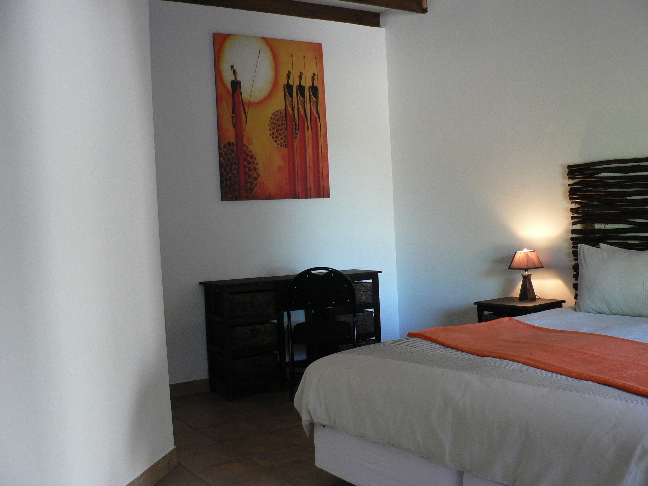 A bedroom with a bed, a desk, a lamp, and a painting on the wall.