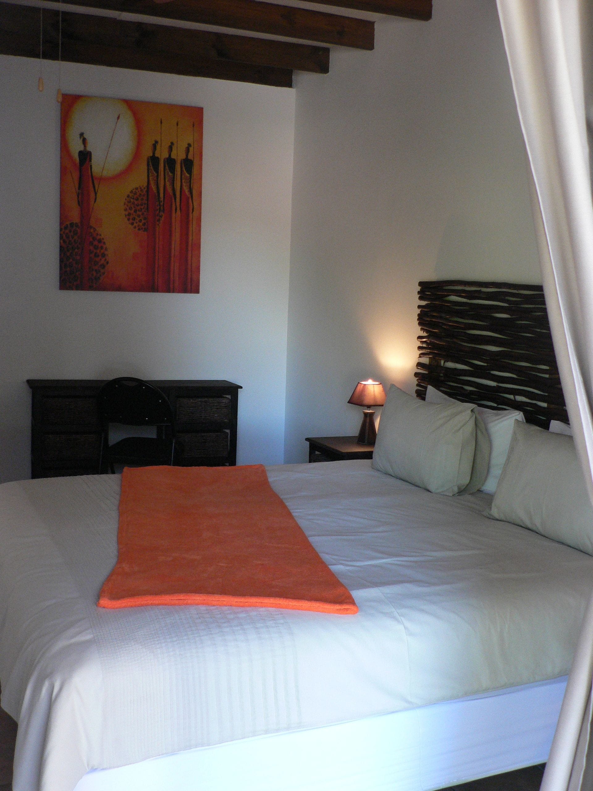 Quarto com cama, mesa de cabeceira com abajur, pintura na parede e cabeceira de madeira.