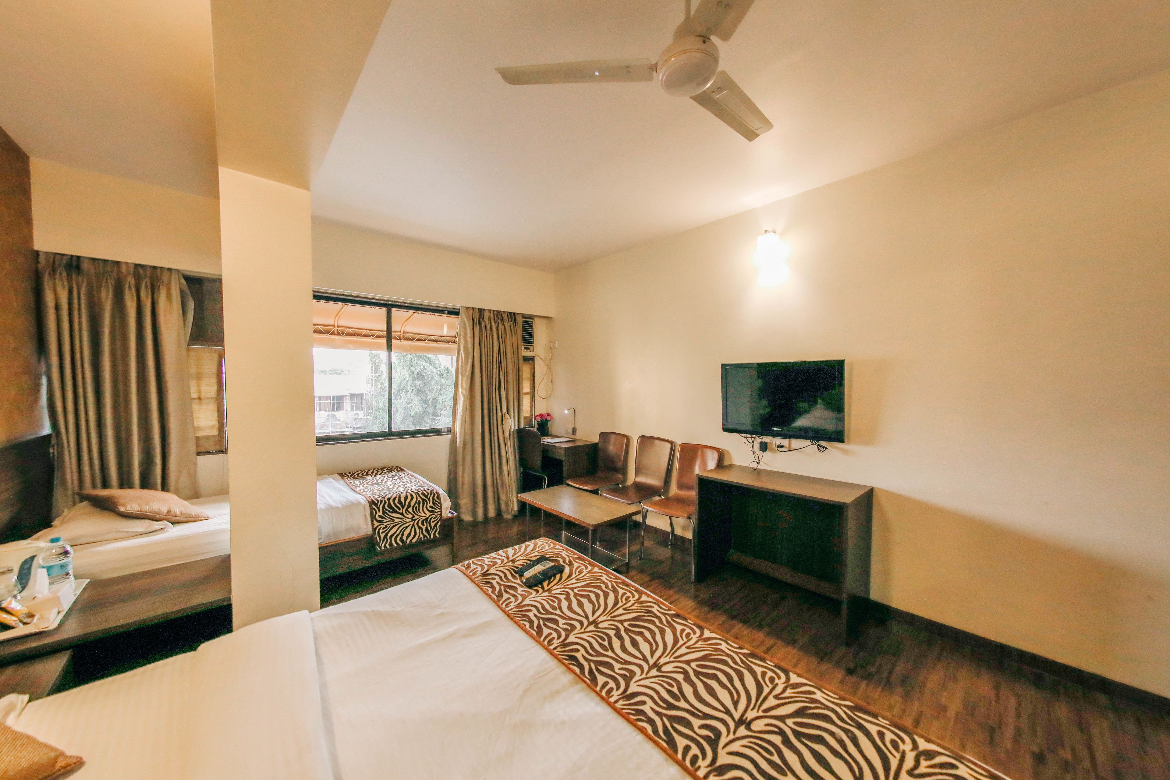 A hotel room with a bed, a desk, a television, and a window with curtains.