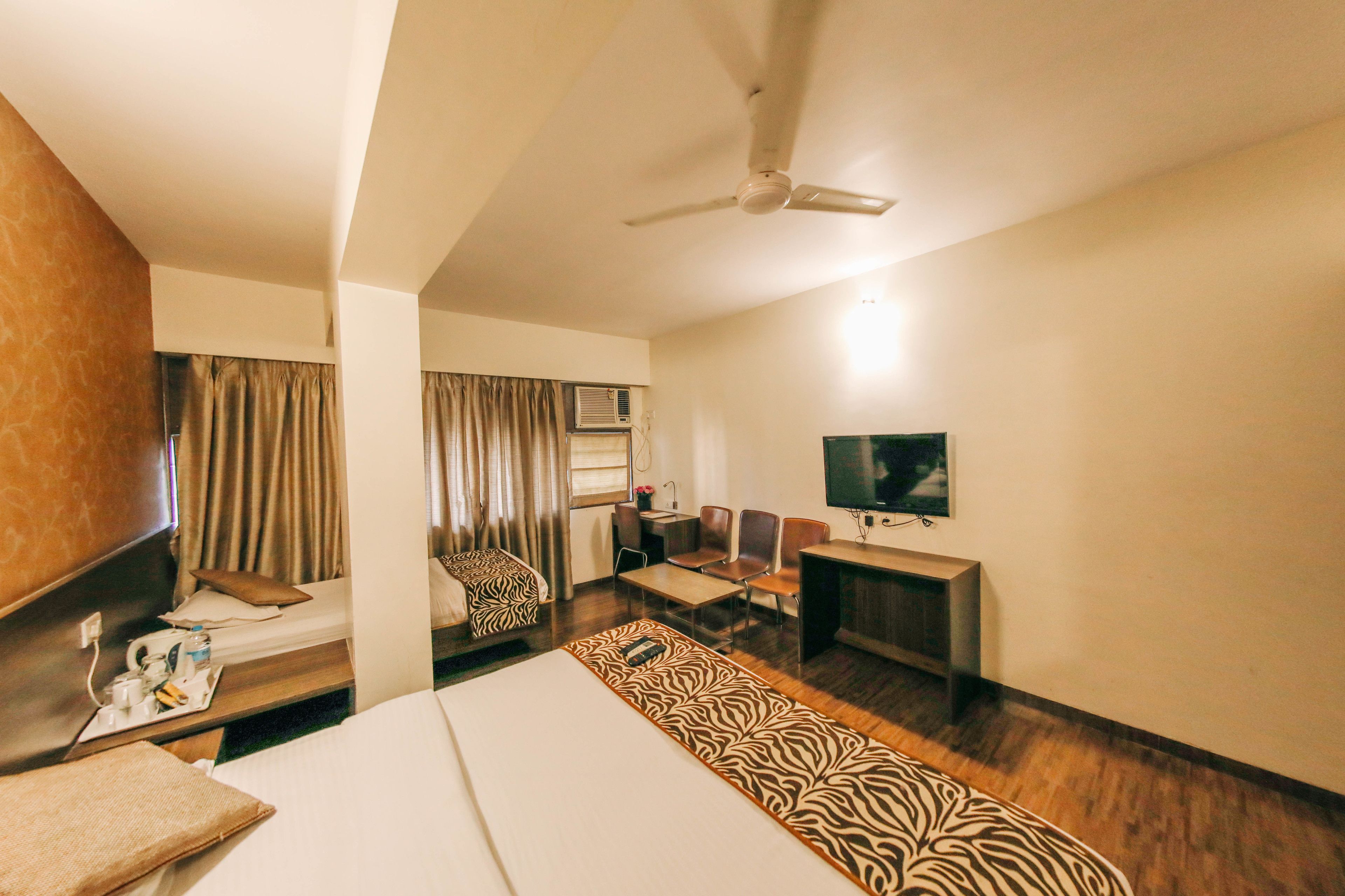A hotel room with a bed, a desk, a chair, a television, and a ceiling fan.