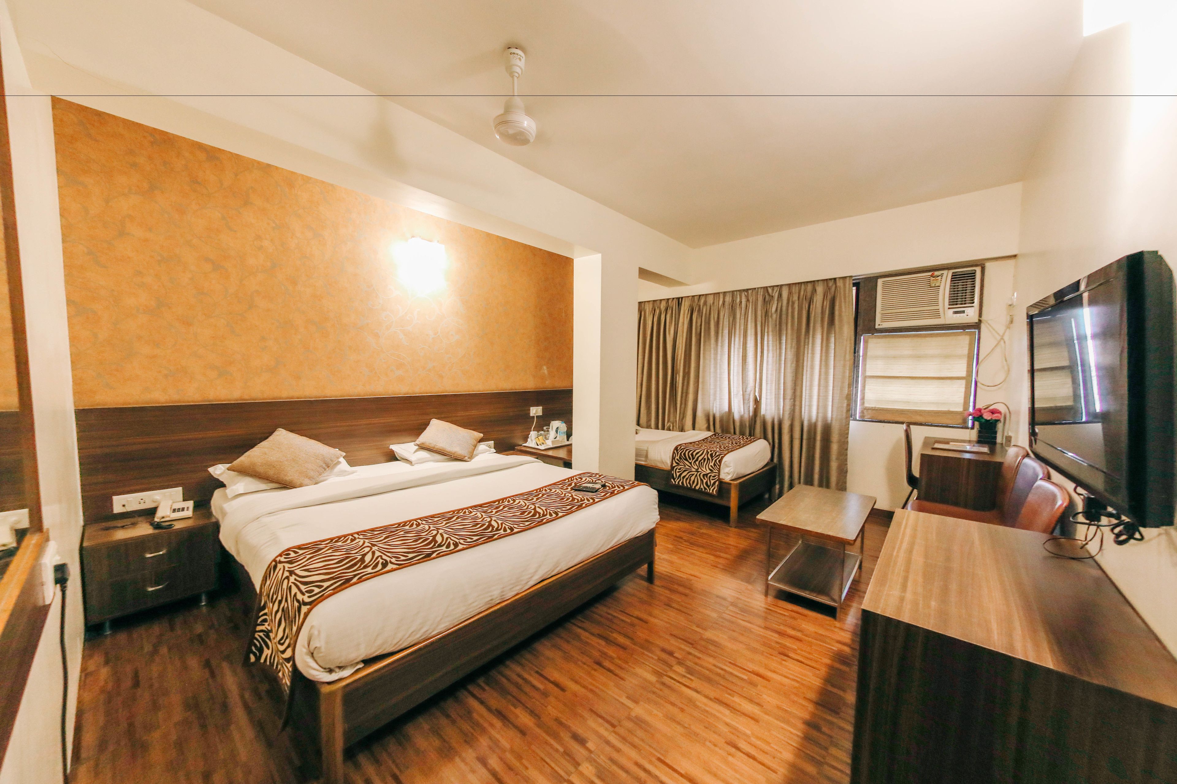 Quarto de hotel com uma cama grande, uma cama menor, uma escrivaninha e uma televisão.