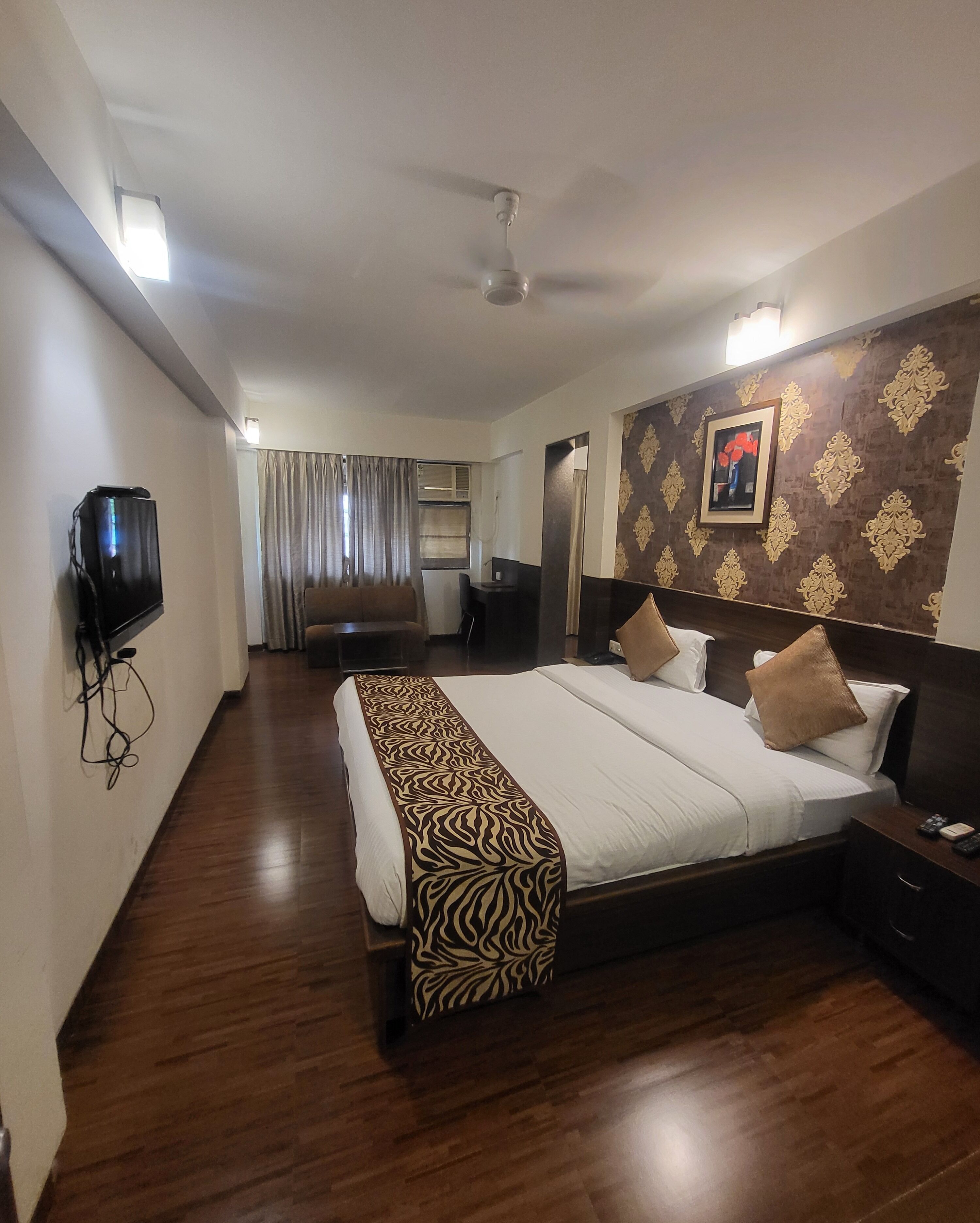 Une chambre d’hôtel avec un grand lit, un téléviseur fixé au mur, un ventilateur de plafond et un papier peint à motifs.