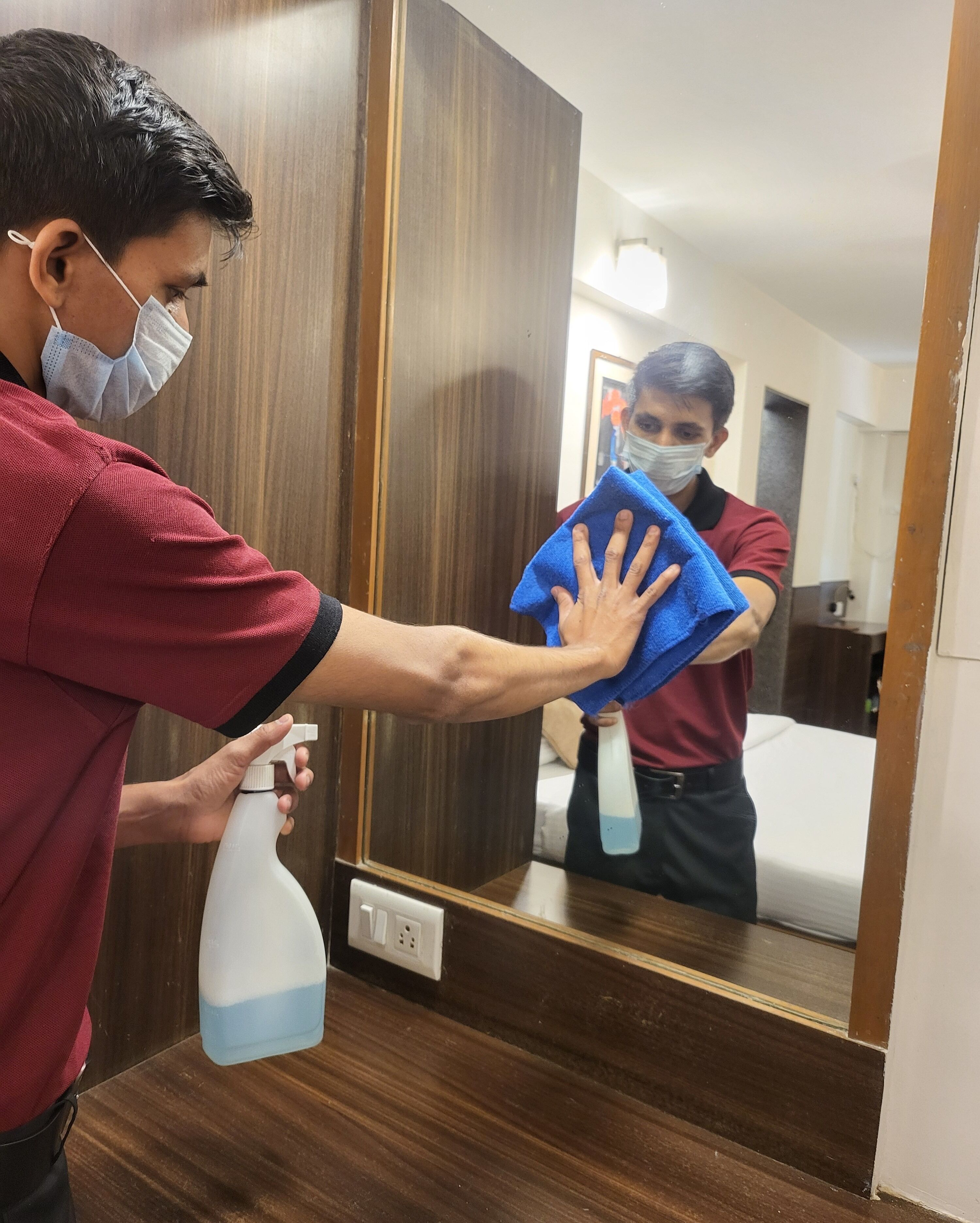 Una persona pulisce un pavimento di legno con un flacone spray e un panno blu.