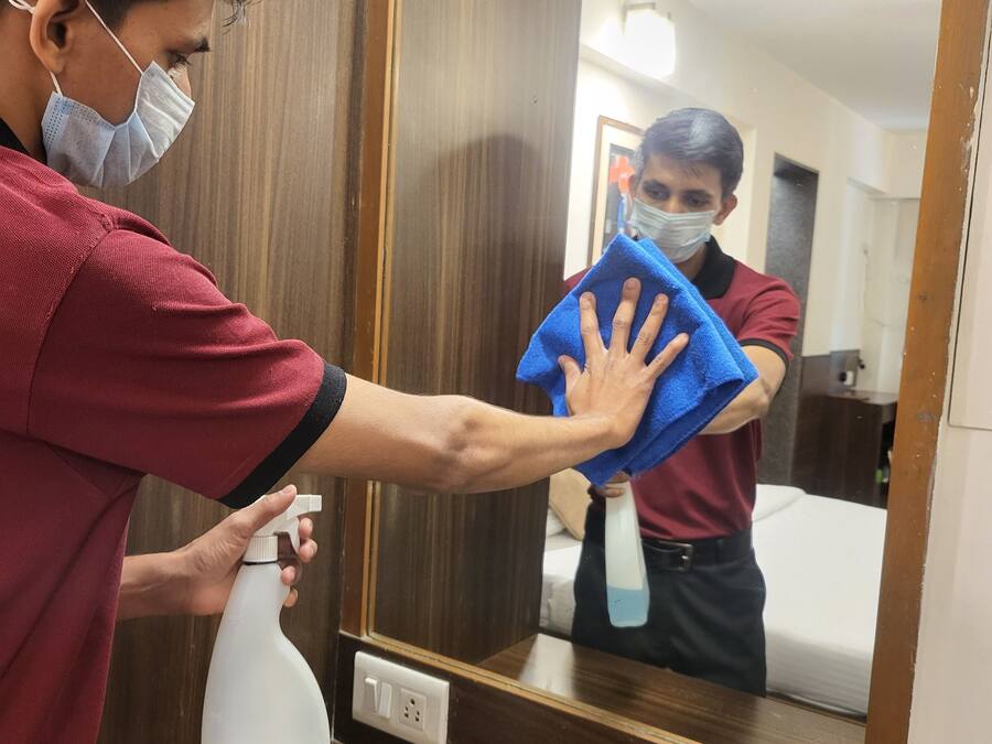 Una persona pulisce un pavimento di legno con un flacone spray e un panno blu.