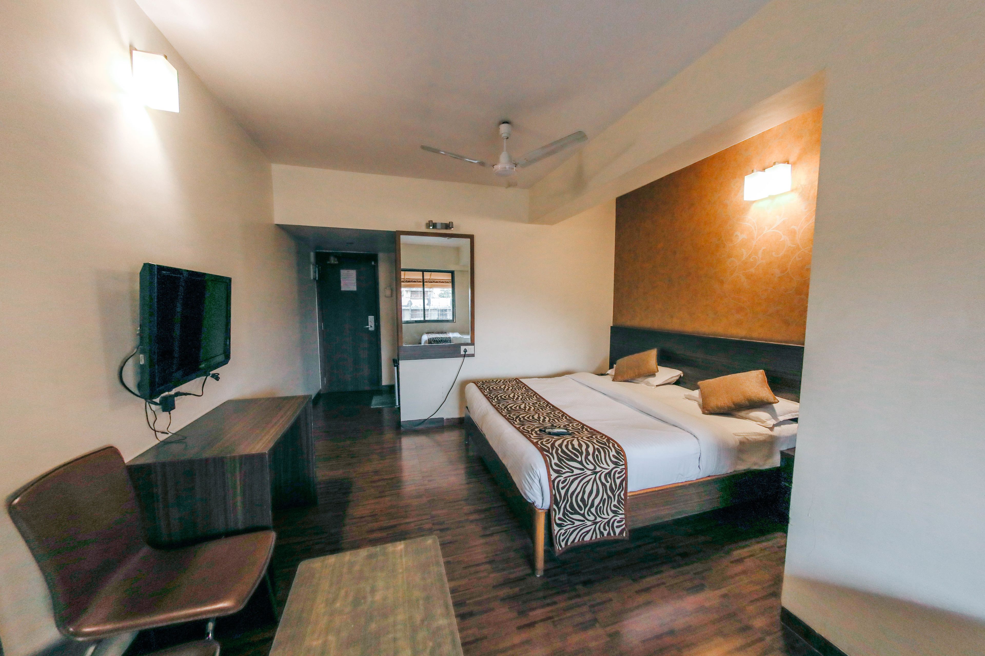 A hotel room with a bed, a desk, a chair, a television, and a ceiling fan.