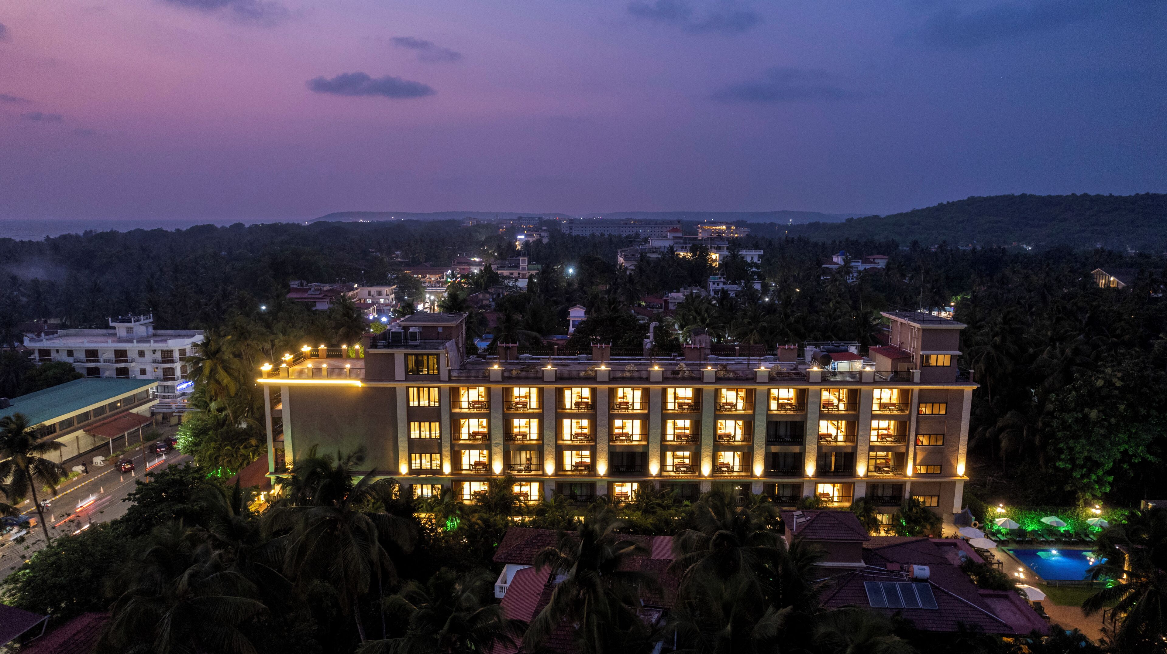 A multi-story hotel with a pool area, surrounded by palm trees and a hilly landscape.