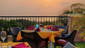 Mesa preparada para comer con vistas a la puesta de sol, sillas exteriores y una barandilla.